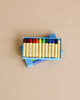 A box of Stockmar Wax Stick Crayons with various colors ranging from red to blue, neatly arranged and displayed on a light beige background.
