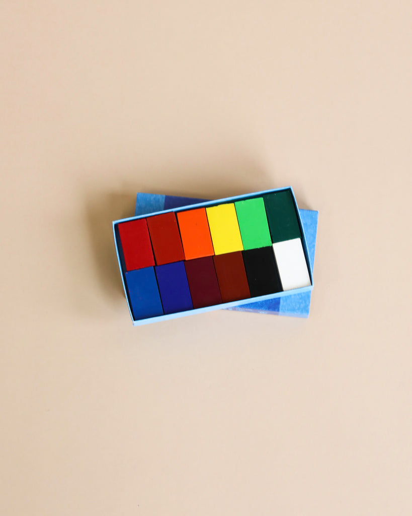 An open Stockmar Crayon Set with a Wooden Organizer Tray displays vibrant colors like red, orange, yellow, green, blue, and black on a beige background. The crayons are neatly arranged in two rows, perfect for meeting artistic demands.
