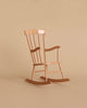 A small wooden rocking chair with a simple, classic design sits against a beige background. The Maileg Rocking Chair, Mini - Dark Powder (Larger Size) features vertical slats on the backrest and contoured armrests, with gently curved rockers completing the charming look.