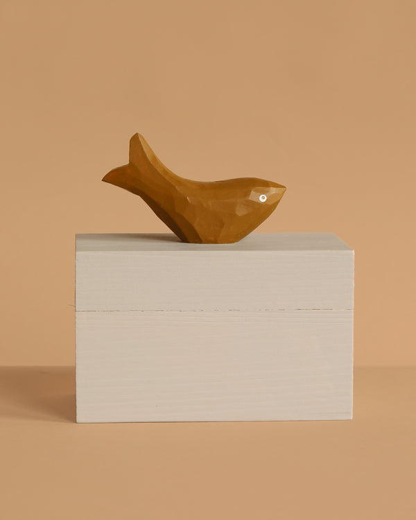 The Ferm Living Hand Carved Wooden Harbour Box - Fish features a small, brown wooden fish with a simple design on a hand-carved box, making it a charming decor piece for children's rooms against a beige background.