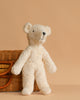 A soft, cream-colored Senger Naturwelt Stuffed Animal - White Bear stands upright by a wicker basket with curved handles on a beige background—a perfect sustainable addition to any nursery.