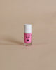 A small pink Nailmatic kids nail polish bottle with a cute face design on a beige background. The cap is white.