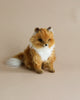 A realistic Sitting Fox Stuffed Animal sitting upright against a plain beige background, with detailed fur in shades of brown and white and an alert, attentive expression.