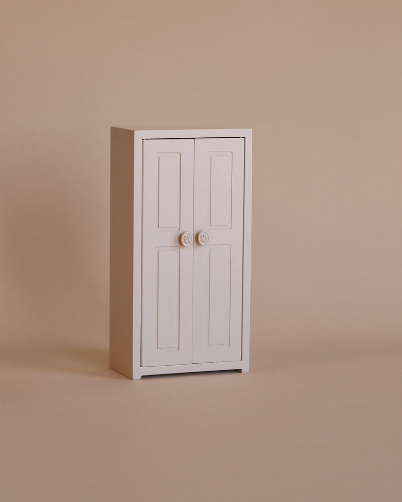 The Maileg Nursery Set with Brothers and Sisters features a small white two-door cabinet, perfect for storing tiny treasures or accessories for Maileg mice and their matchbox beds, displayed against a plain beige background.