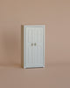 The Maileg Mum Mouse Wardrobe Set, a compact white closet with double doors and round knobs for storing mice clothes, stands on a plain beige surface with a beige background.