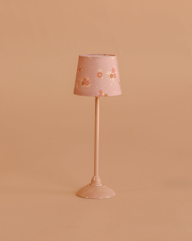 The Maileg Floor Lamp, Miniature - Dark Powder features a small pink stand and floral-patterned lampshade, making it perfect for dollhouse decor. Displayed against a simple beige background.