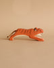A wooden Ostheimer Jumping Tiger painted in orange with black stripes is shown against a beige background. The tiger, perfect for imaginative play, is in a prowling position with an open mouth and features a rope tail. Handcrafted with care, this piece embodies the quality of Ostheimer toys.
