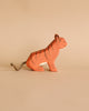 The Ostheimer Handmade Wooden Safari Animals Set features a small, handcrafted wooden tiger figurine with painted orange and black stripes and a yarn tail, perfect for imaginative play, shown against a plain beige background.