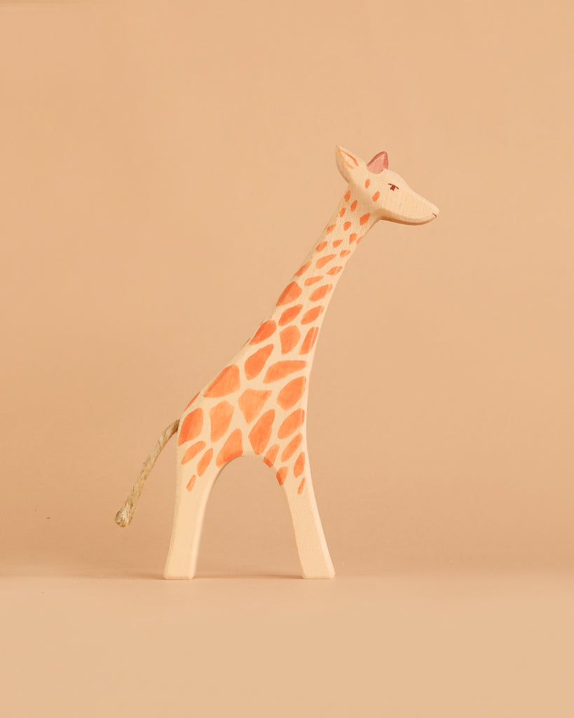The Ostheimer Giraffe - Standing is a small, minimalist wooden figurine adorned with orange spots, displayed on a beige background. It evokes the timeless charm of handcrafted wooden toys and invites imaginative play.