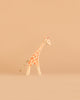A small, minimalist giraffe figurine with orange spots and a rope tail stands on a plain light brown background, inspired by the timeless charm of the Ostheimer Handmade Wooden Safari Animals Set and crafted from sustainably sourced wood.