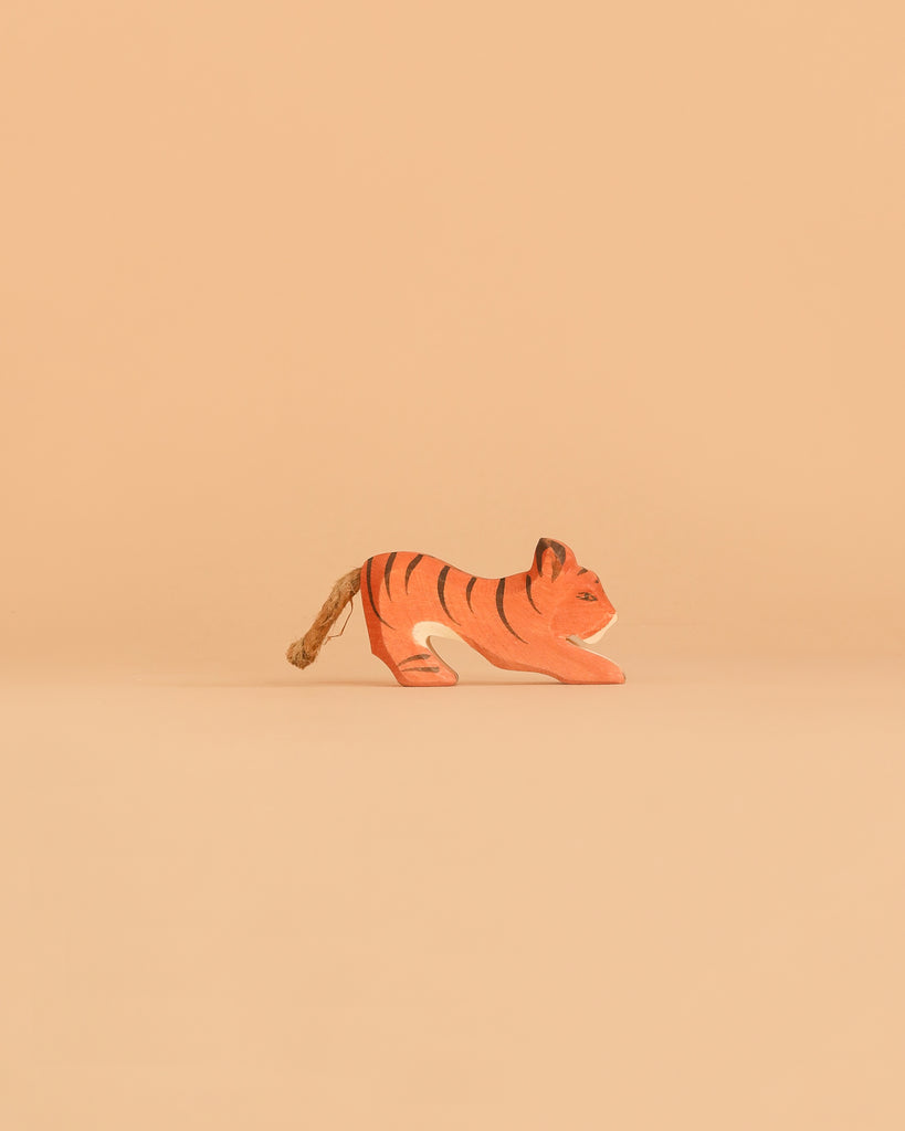 A small handcrafted wooden tiger figurine from the Ostheimer Handmade Wooden Safari Animals Set, painted with orange and black stripes, stands on a light beige background—highlighting the charm and sustainability of these unique toys.