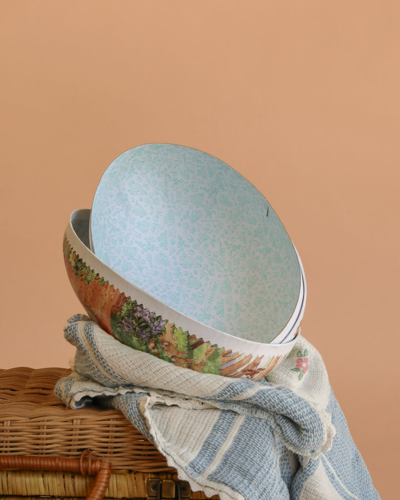 An extra large Cardboard Beatrix Potter Egg featuring Mother Rabbit with three baby rabbits rests on a woven basket draped in a cream and blue striped cloth, adding handcrafted charm to the soft beige background.