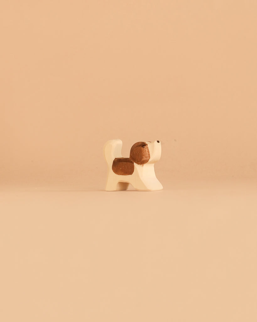 An adorable member of the Ostheimer Handmade Wooden Dog Family Set stands on a plain beige background, its minimalist, handcrafted wooden design and sustainably sourced materials echoing the charming simplicity for which Ostheimer toys are renowned.