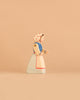 Introducing the Ostheimer Handmade Wooden Swan Girl Set: a beautifully handcrafted wooden figurine of a woman in a bonnet with red dots, a blue shirt, and a long white skirt, standing on a beige background. Inspired by Ostheimer toys and carefully made from sustainably sourced wood, this set captures the timeless charm of traditional craftsmanship.