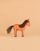 An upright handcrafted wooden horse from the Ostheimer Handmade Wooden Farm Animals Set, featuring a brown body with a black mane and tail, stands against a light beige background. Expertly crafted from sustainably sourced materials, this charming figure exemplifies the enduring quality characteristic of Ostheimer toys.