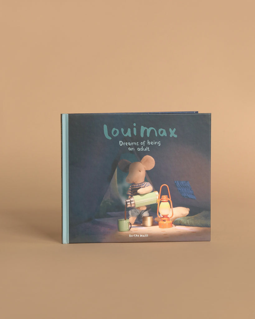 The Maileg LouiMax Storytime Family Set is displayed upright against a beige background, featuring an illustrated mouse with Maileg accessories like a kettle and lantern sitting in a tent on the cover.