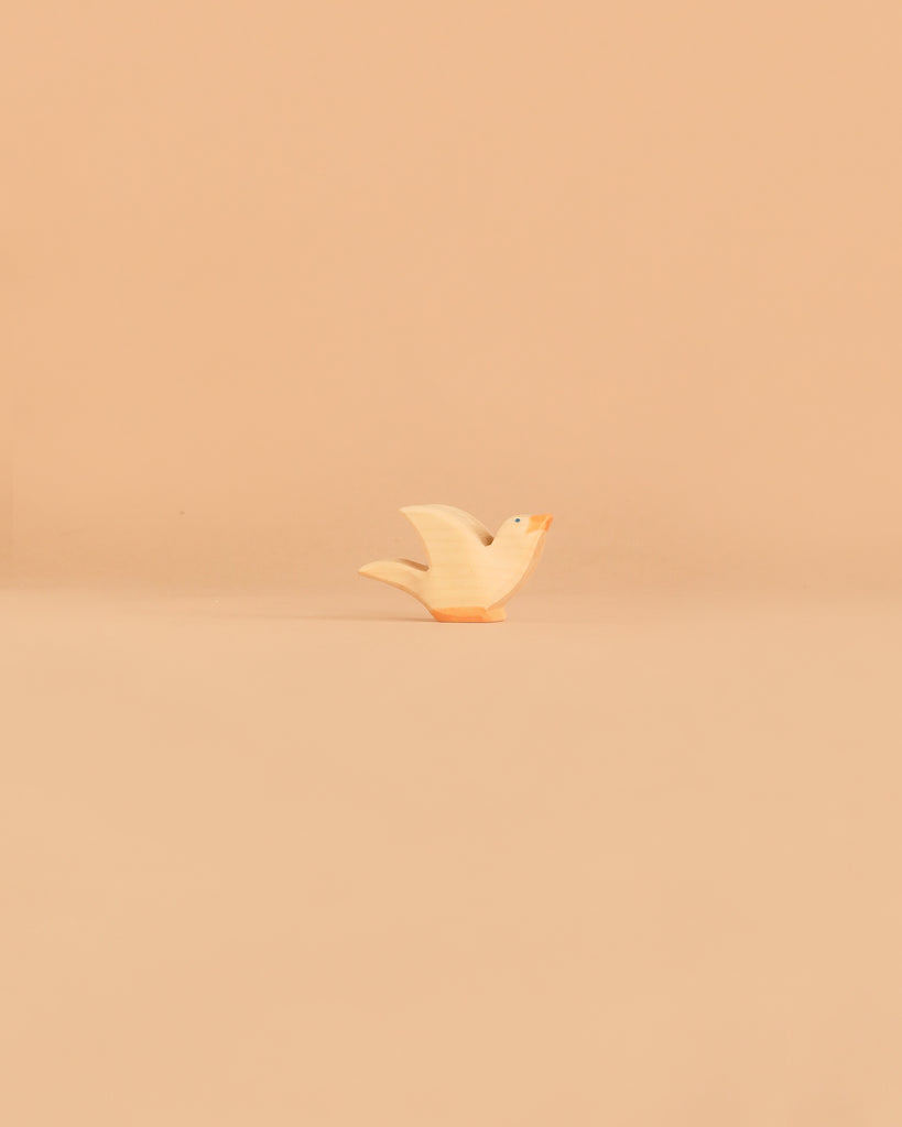 A small, white Ostheimer Bird - Flying Dove figurine with an orange beak stands on a pale beige surface against a matching plain background, reminiscent of the charming handcrafted quality and non-toxic materials for which Ostheimer wooden toys are beloved.