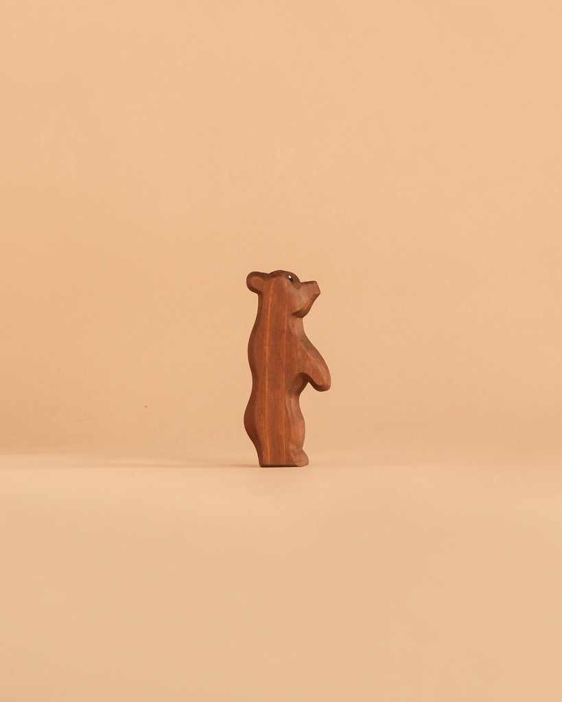 A small, brown bear figurine from the Ostheimer Handmade Wooden Woodland Animals Set stands upright on a plain beige background, embodying the charm and quality of handcrafted toys.