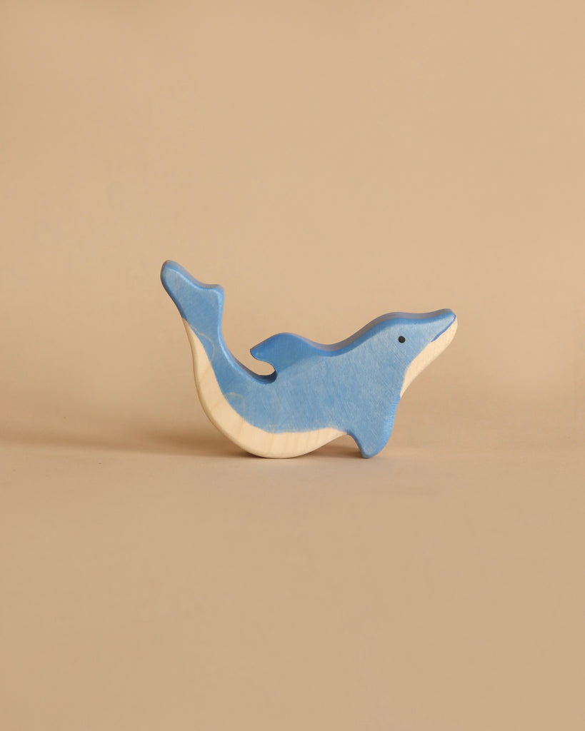 A dolphin from the Holztiger Handmade Wooden Ocean Animals Set, painted blue on top and white underneath, stands upright against a plain beige background.