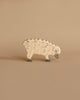 A small wooden toy resembling a sheep, handcrafted wood and painted beige with darker curved lines representing wool texture. The high-quality Holztiger Sheep, Eating stands on a neutral beige background, and its simple design includes a gray snout and feet, reminiscent of HOLZTIGER figures.
