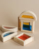 Four Wooden Water Blocks with colorful, translucent acrylic centers in shapes of arches and rectangles, arranged on a beige surface.