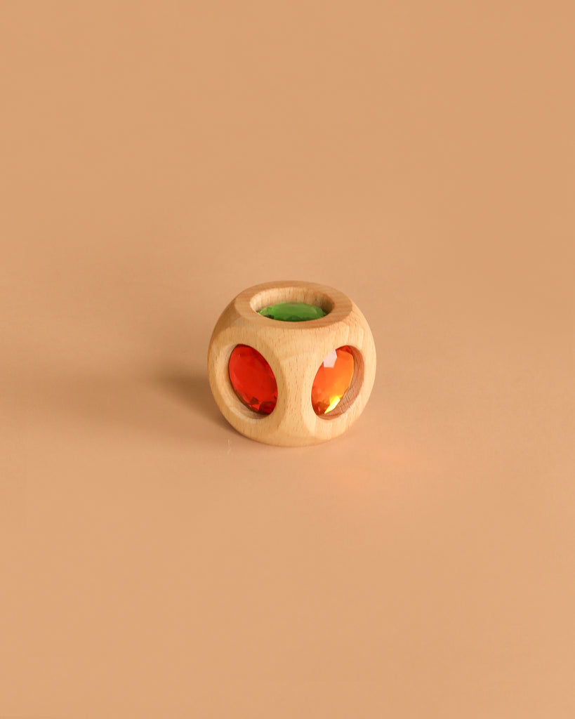 The Bauspiel Magic Cube (Single) is a small wooden toy with circular cutouts, featuring green and red translucent gems. It rests on a plain beige background—ideal for pairing with other wooden building blocks or educational sets.