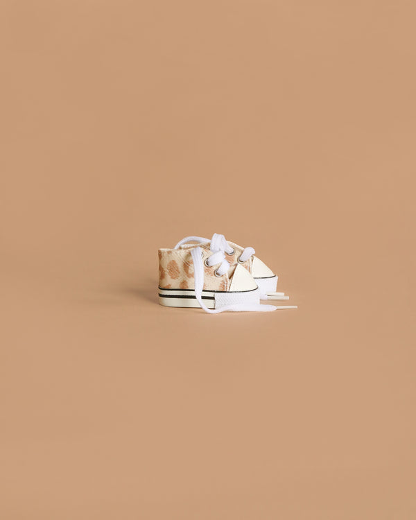 Minikane Doll Shoes | Converse Style Feline Print Sneakers are small, beige sneakers with white laces and soles—ideal footwear for 34cm-37cm dolls, shown on a light brown background.