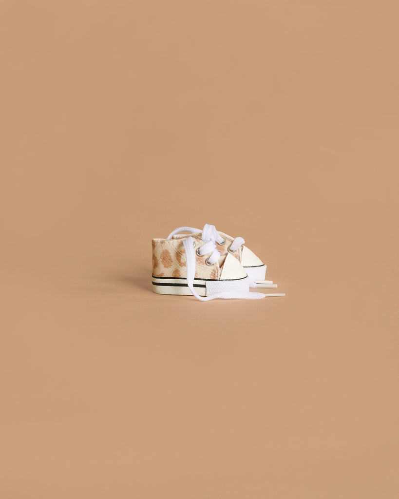 Minikane Doll Shoes | Converse Style Feline Print Sneakers are small, beige sneakers with white laces and soles—ideal footwear for 34cm-37cm dolls, shown on a light brown background.