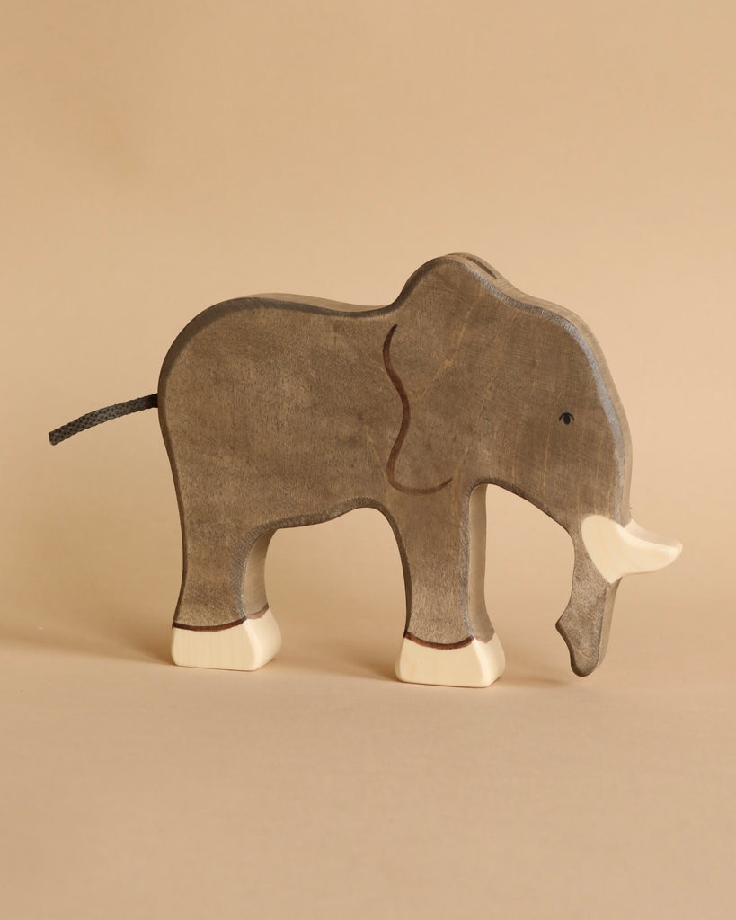 A Holztiger Handmade Wooden Safari Animals Set elephant, hand-painted in gray and white, stands on a beige surface. Its simple handcrafted details inspire imaginative play in any environment.