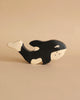 A Holztiger Handmade Wooden Sea Animals Set orca whale toy, crafted from maple and beech wood and painted black and white, is displayed on a beige surface with a matching beige background.