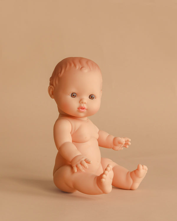 The Minikane Vintage Baby Doll (13") - Faustine sits upright on a beige background. This anatomically correct, light-skinned doll with brown eyes and short molded hair is made in Spain. Clothing sold separately.