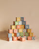 A pyramid of Uncle Goose Classic ABC Blocks neatly stacked against a light beige background, featuring a variety of letters and symbols in a playful font on wooden toys.