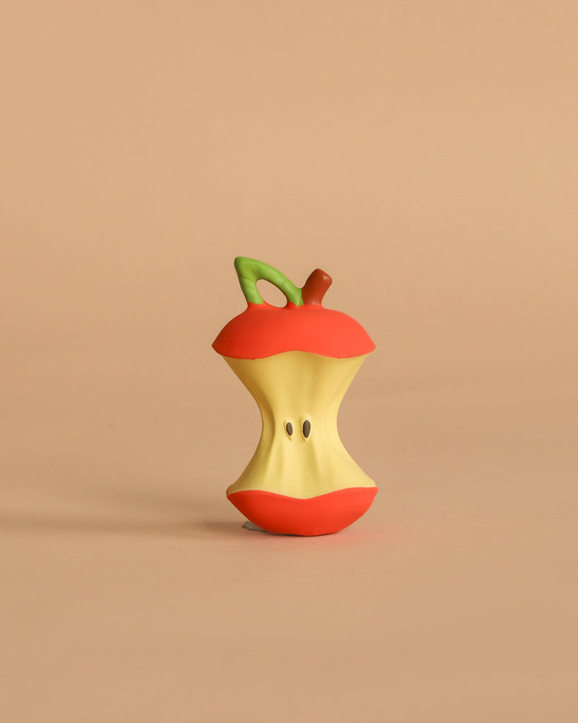 Pepa the Apple Teething Toy is an eco-friendly, cartoonish apple core with red skin, a green stem, and two seeds. It stands upright on a beige surface and features exaggerated details, making it perfect for bath time fun.