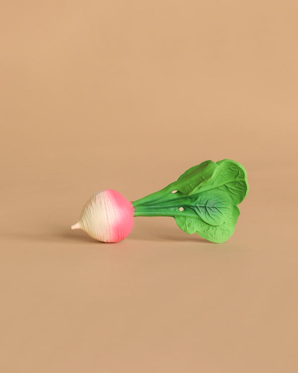 Ramona the Radish Teething Toy, featuring green leaves and a white-and-pink root, rests on a plain beige background—an ideal natural rubber baby toy for sensory play.