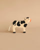 A Holztiger Handmade Wooden Black & White Cow Family Set, featuring a handcrafted wooden cow with black spots, a pink snout, and a rope tail, perfect for imaginative play.