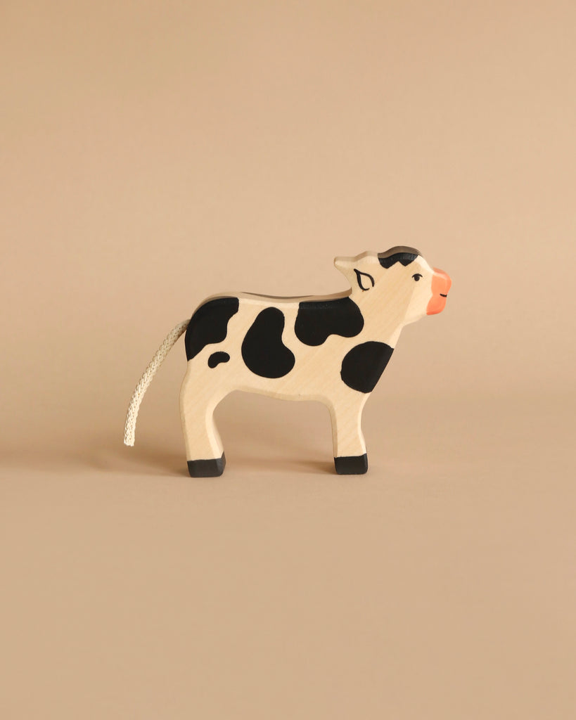 A Holztiger Handmade Wooden Black & White Cow Family Set, featuring a handcrafted wooden cow with black spots, a pink snout, and a rope tail, perfect for imaginative play.