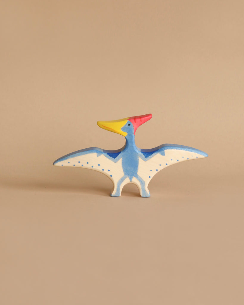 Handmade Holztiger Wooden Dinosaur Set pterodactyl toy with a blue body, white wing undersides with blue spots, and a red and yellow head, perfect for imaginative play.
