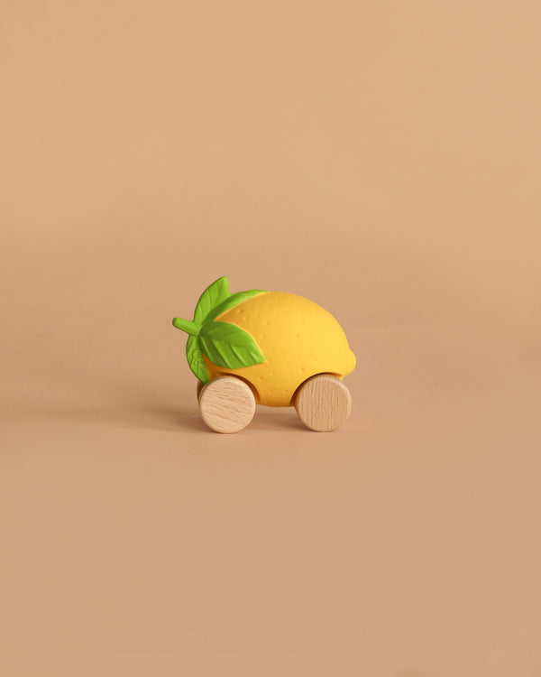 Lou The Lemon Baby Car, an eco-friendly toy shaped like a yellow lemon with green leaves and two round wooden wheels, is set against a plain beige background.