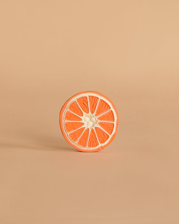 A single round slice of orange grapefruit with a white rind sits upright on a light beige background, echoing the design of Clementino the Orange Teething Toy—a natural rubber baby toy for teething and sensory play.
