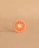 A single round slice of orange grapefruit with a white rind sits upright on a light beige background, echoing the design of Clementino the Orange Teething Toy—a natural rubber baby toy for teething and sensory play.