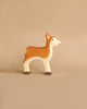 A minimalist wooden figurine of a deer, handcrafted in Europe by Holztiger Deer, is set against a simple beige background. The figurine is painted with a brown and white color scheme, capturing a graceful yet simplistic design.
