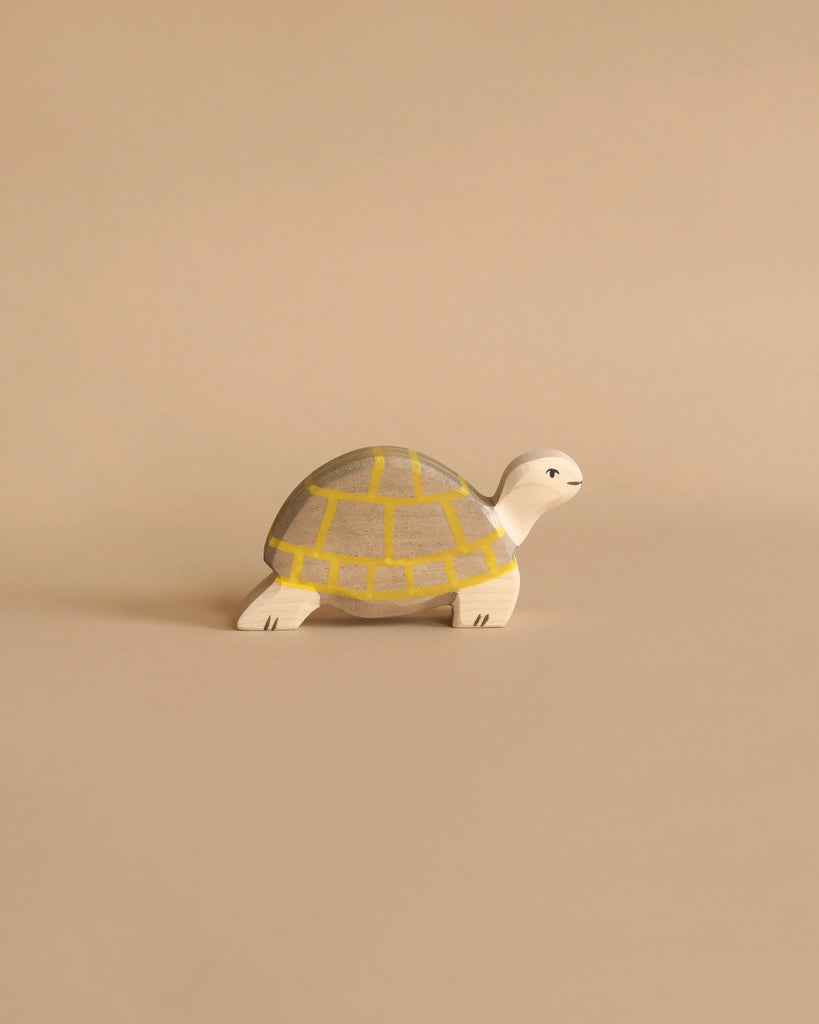 The Holztiger Handmade Wooden Sea Animals Set includes a maple and beech wood turtle figurine with a yellow and gray shell, displayed on a beige surface that matches its charming artisanal style.