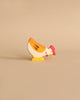 A small, colorful wooden figurine of a hen stands on a plain beige background. Handcrafted out of maple and beech wood, this Holztiger Hen, Pecking figure is painted with yellow, white, and orange body parts and has a red comb on its head. The simple, cartoonish design adds a playful touch to the figurine.