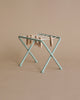 A small green Maileg Miniature Drying Rack with a string tied across its top, holding several wooden clothespins, is displayed against a plain beige background. Ideal for dollhouses or organizing small parts.