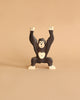 A dark brown and beige wooden gorilla toy from the Holztiger Handmade Wooden Safari Animals Set stands with both arms raised against a plain beige background, highlighting the charm and craftsmanship of these handmade safari animals.