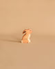 A small wooden figurine of a rabbit, portrayed in a sitting position, is placed against a neutral beige background. This Holztiger Rabbit, Sitting is light brown with white accents on its chest and tail. Made in Europe like all HOLZTIGER figures, it exudes quality and charm.
