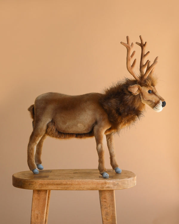 The 20" Brown Reindeer Stuffed Animal stands on a wooden stool against a plain beige background.