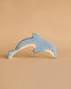 A small blue dolphin from the Holztiger Handmade Wooden Ocean Animals Set has a natural wood underside and is shown against a plain beige background.