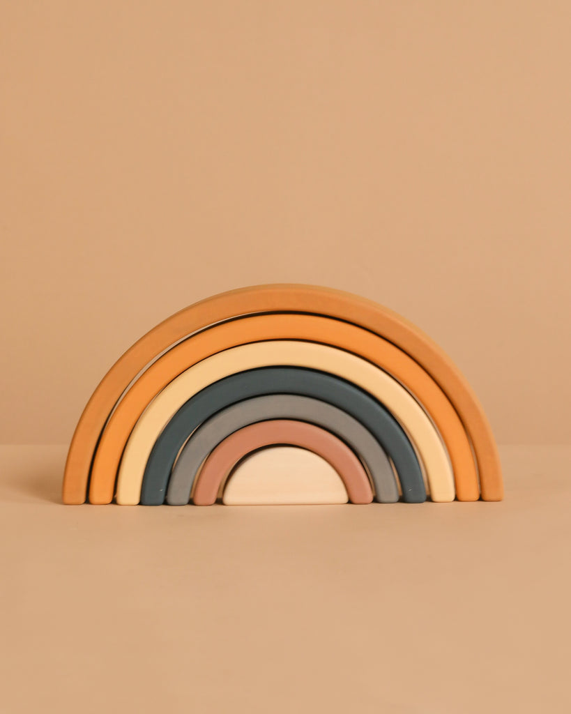The Handmade Rainbow Stacker - Mustard features five wooden arches in muted earth tones, crafted with non-toxic paint for safe play. Arches stack from largest to smallest and are pictured on a beige background.