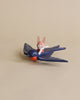 A toy rabbit named Spud the pilot Hare with red ears riding on the back of a toy blue bird named Swifty Bird against a plain beige background. The scene is playful and whimsical.